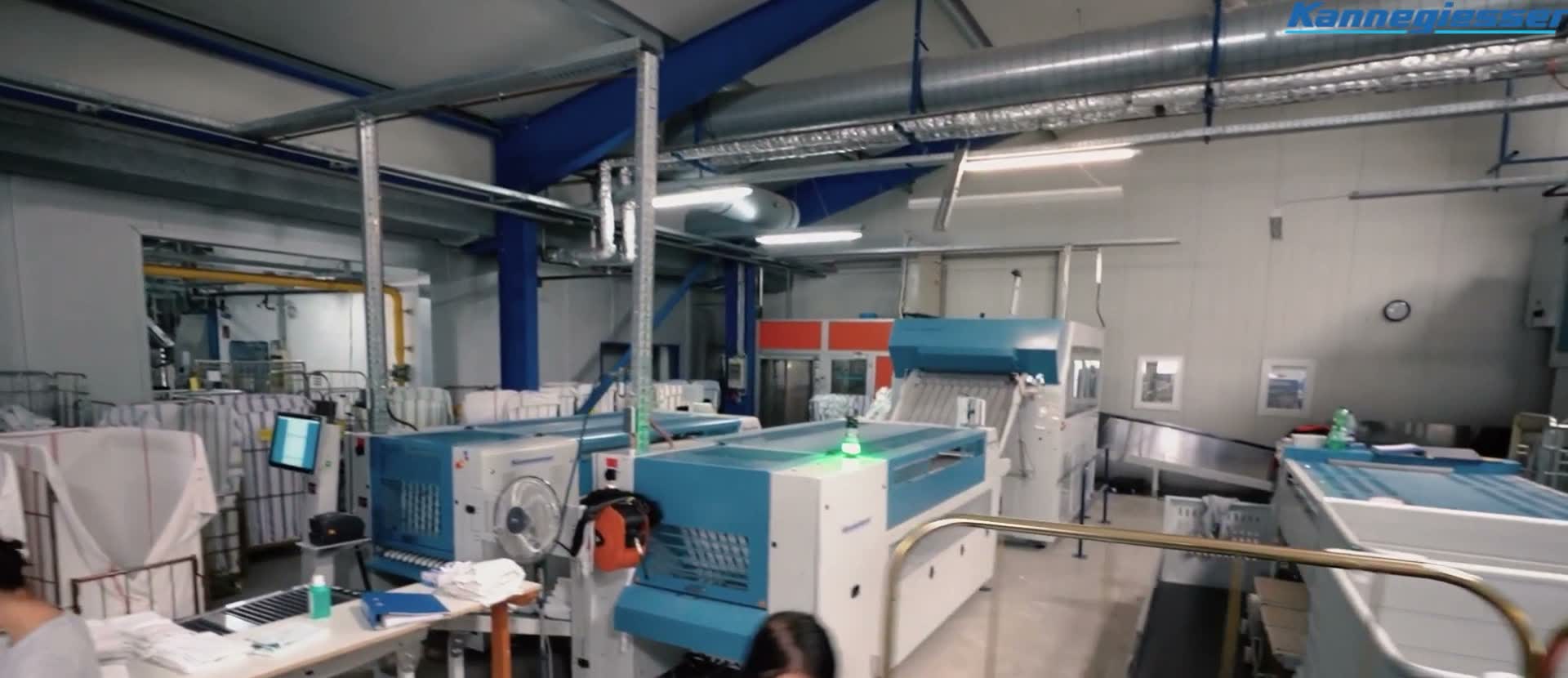 Workers feeding linens into Kannegiesser machines across a wide production floor