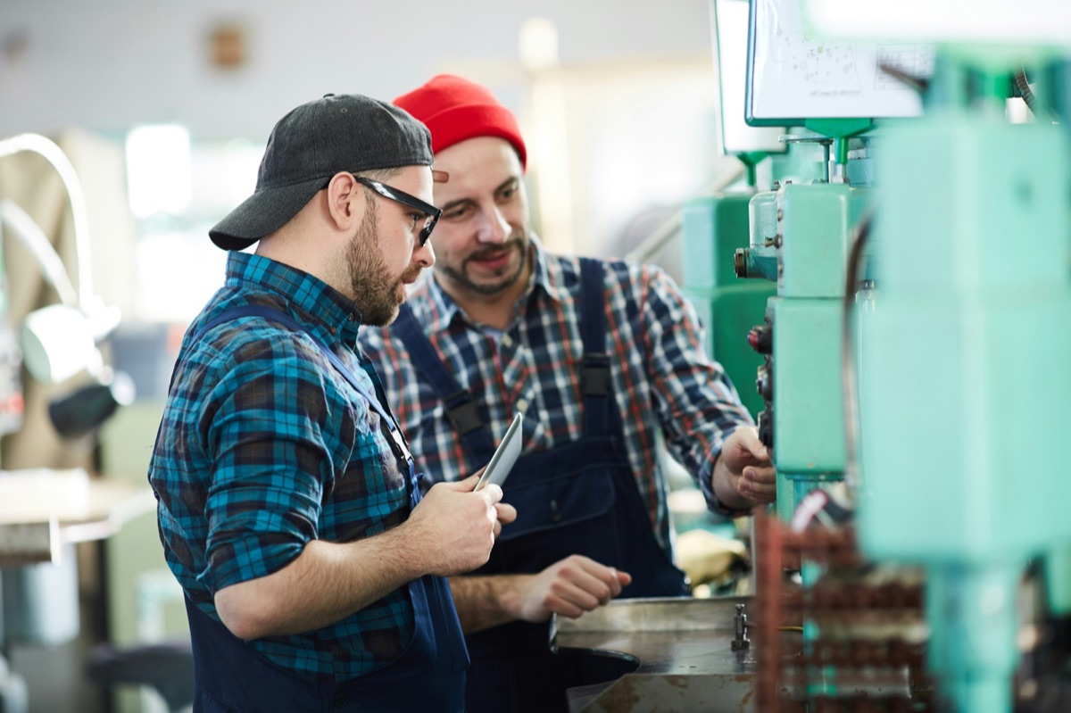 Two workers reviewing a tablet together on the shop floor, answering a new hire's questions