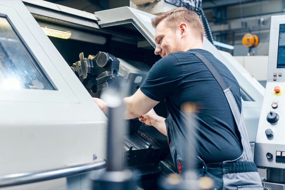 A machinist working a CNC lathe beside its control screen, software running the tools already on the floor