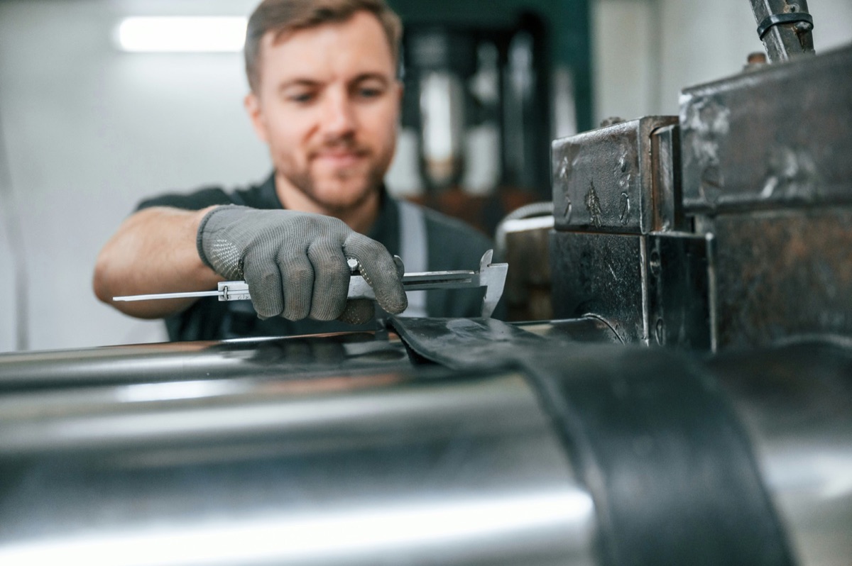A worker measuring a metal part with calipers, verifying quality before it moves downstream